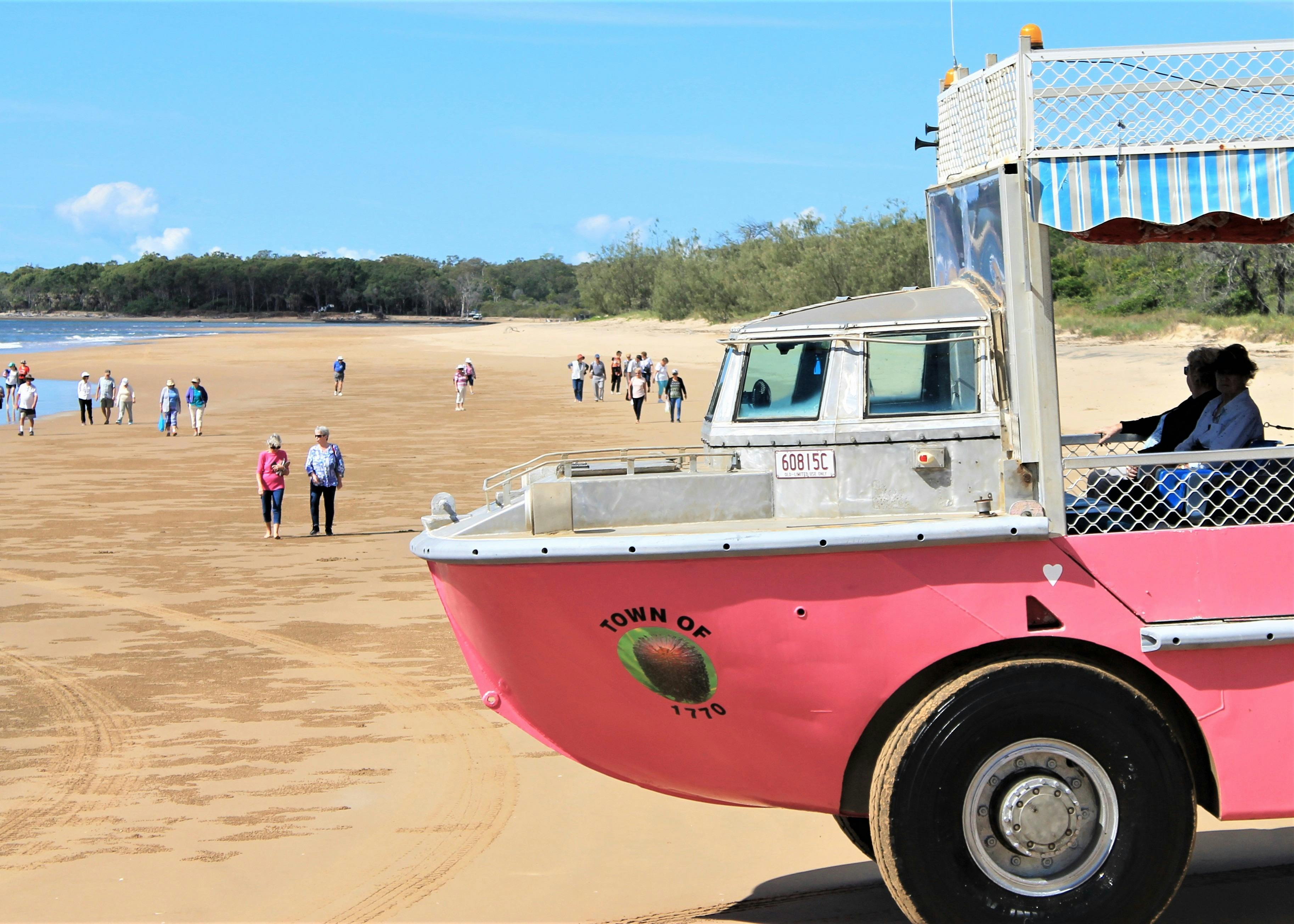 Pink Amphibious Vehicle parked on beach. People are walking the beach.
