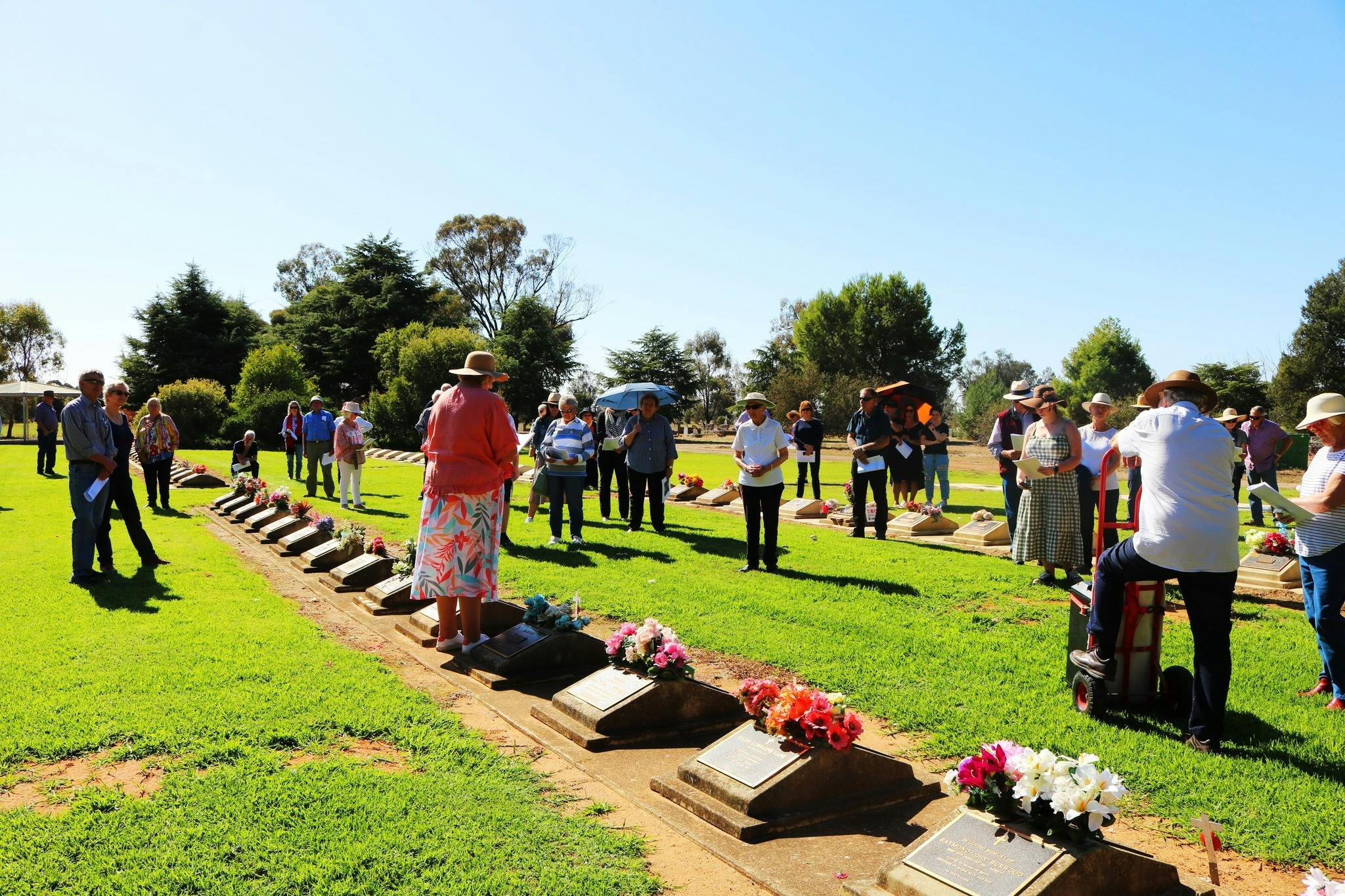 People standing around a lawn cemetery, listening to a speaker