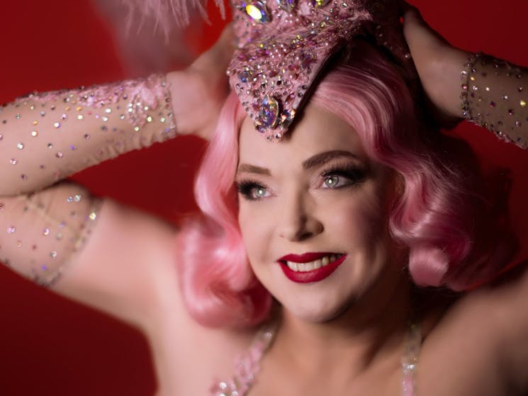 A headshot of performer Dolores Daiquiri, in bright pink flapper attire.