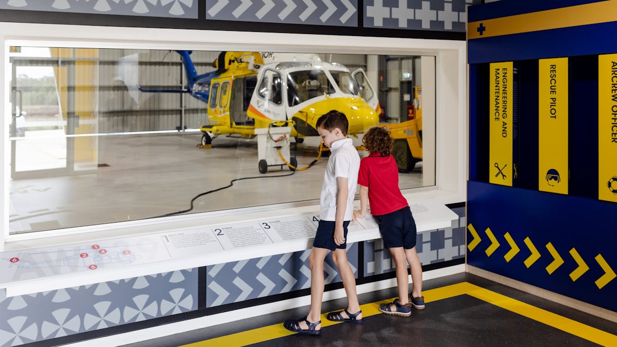 Two kids standing at viewing window with helicopter in hangar