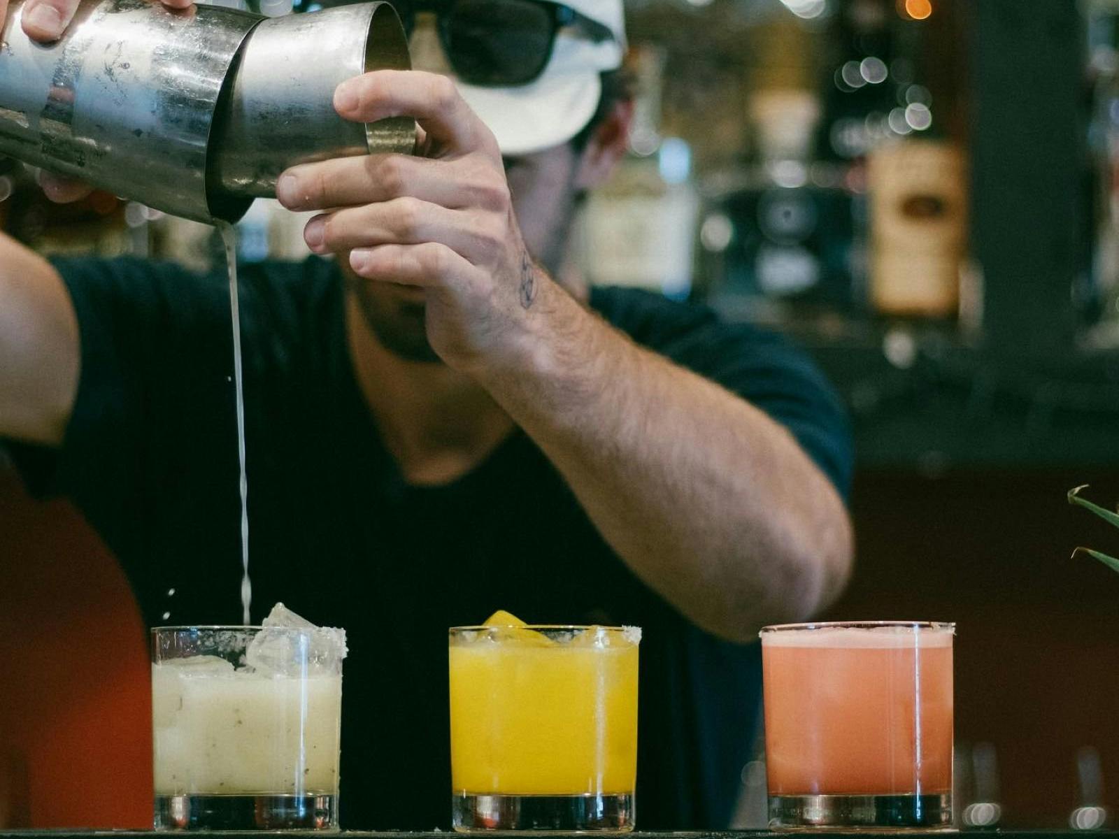 man making three different drinks behind the bar