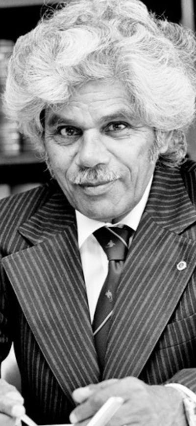 Neville Bonner sitting at a desk with books behind him