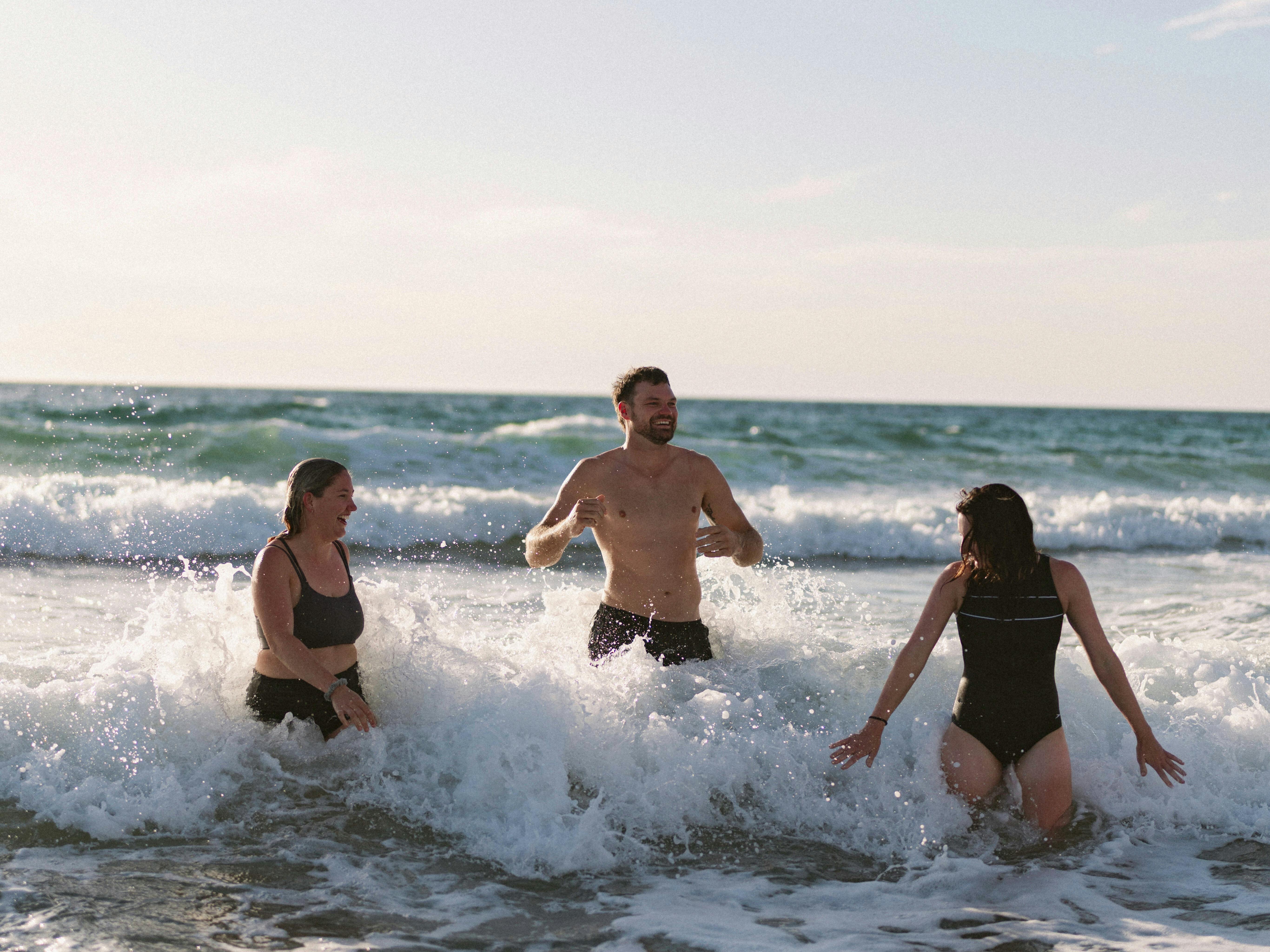 Three people in the white wash of the ocean cooling off after their sauna