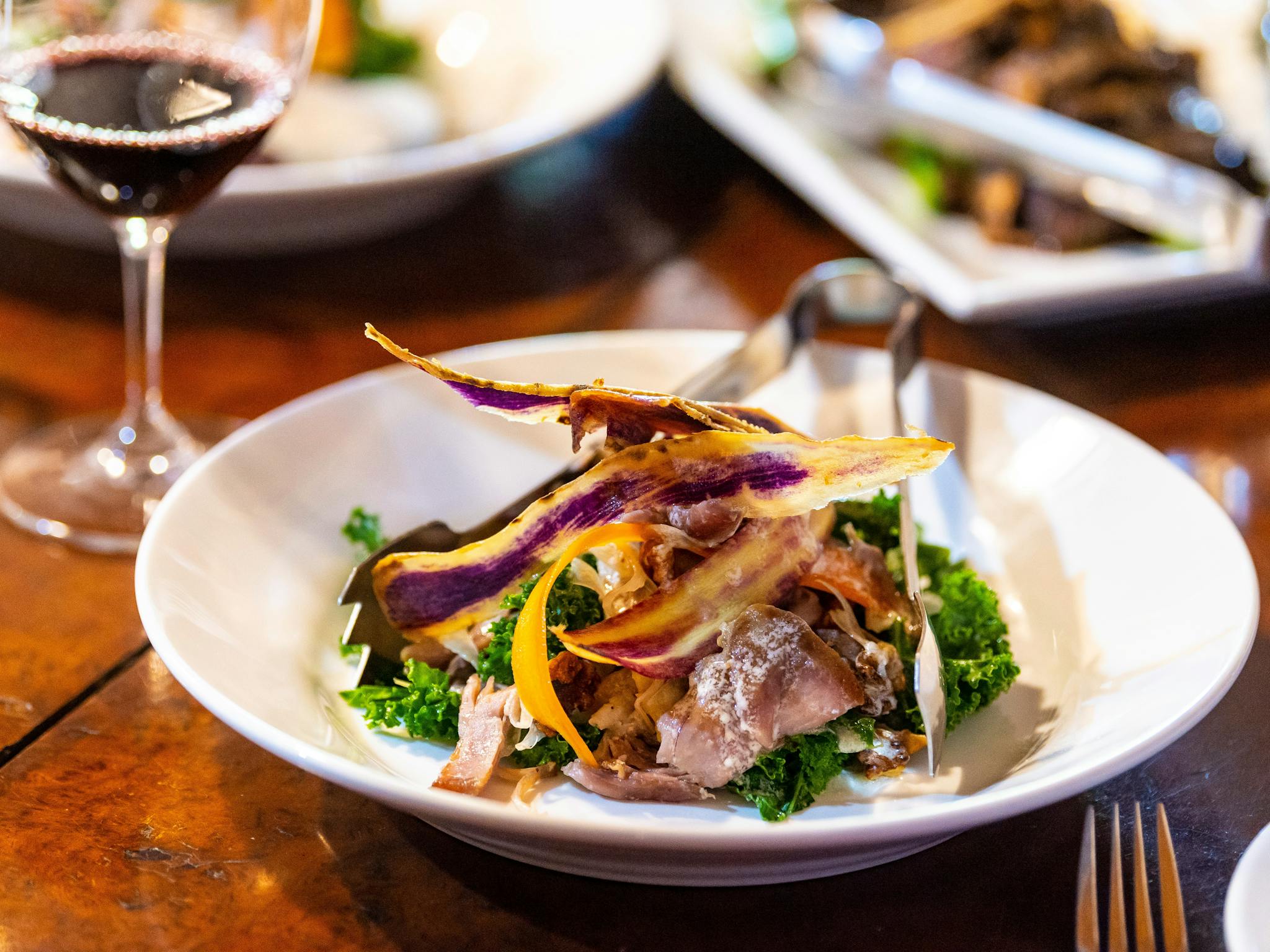 Plate of confit duck salad with other shared plates of food and wine glasses
