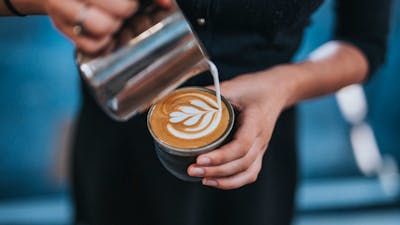 Barista wearing black pouring milk into a coffee cup