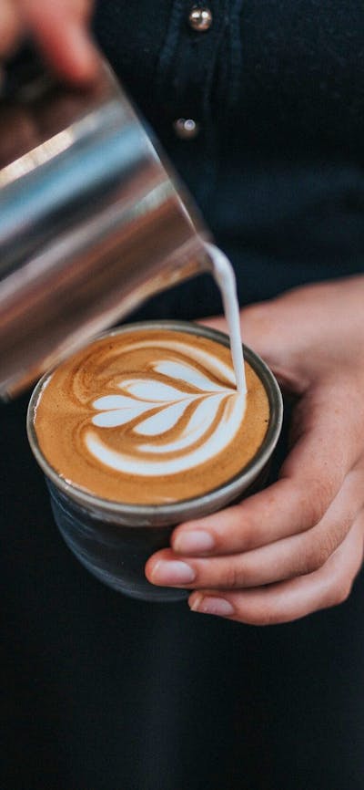 Barista wearing black pouring milk into a coffee cup