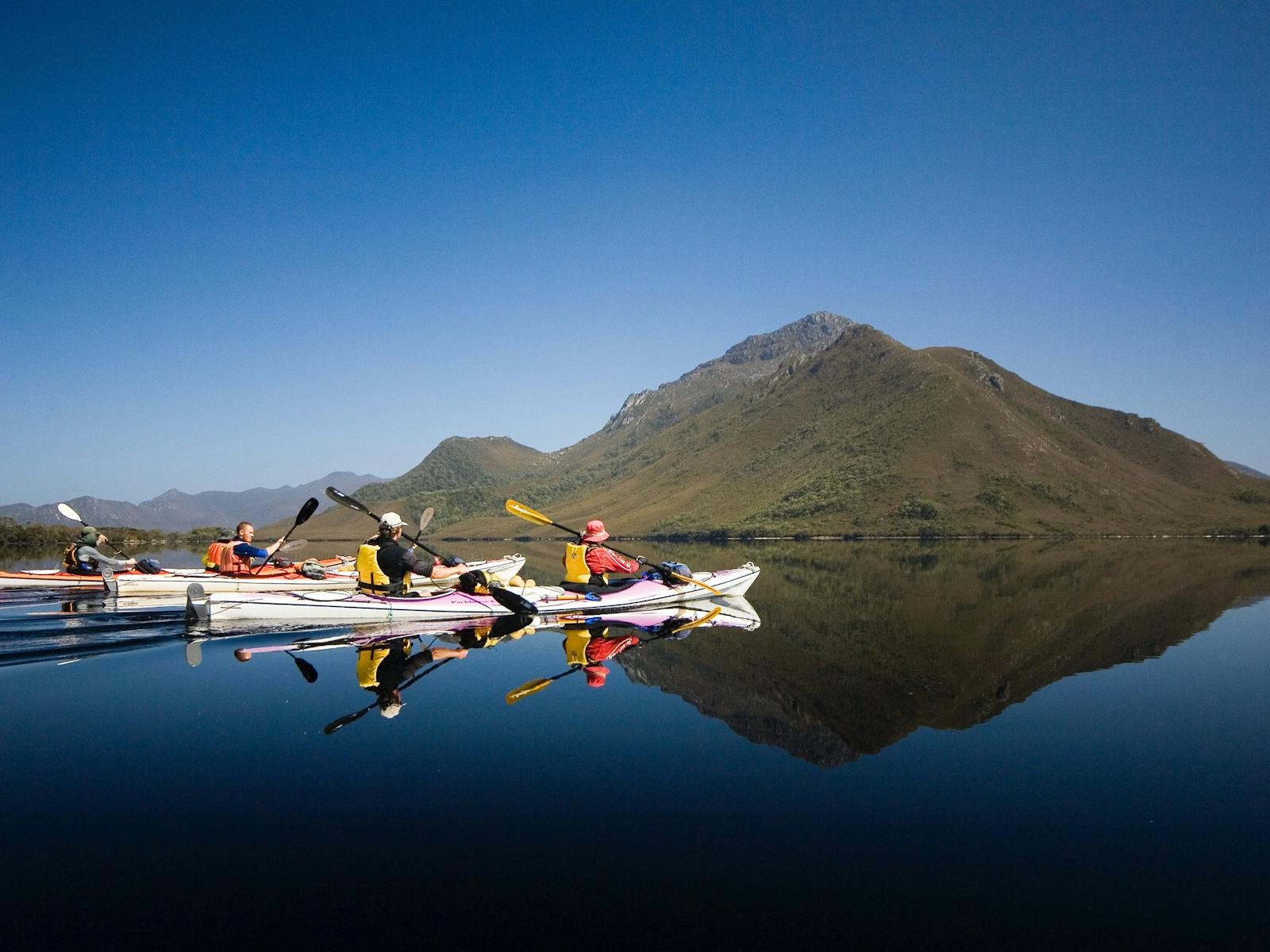 Kayakers paddling in perfect reflections in Southwest Tasmania