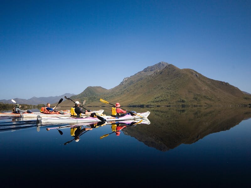 Kayakers paddling in perfect reflections in Southwest Tasmania