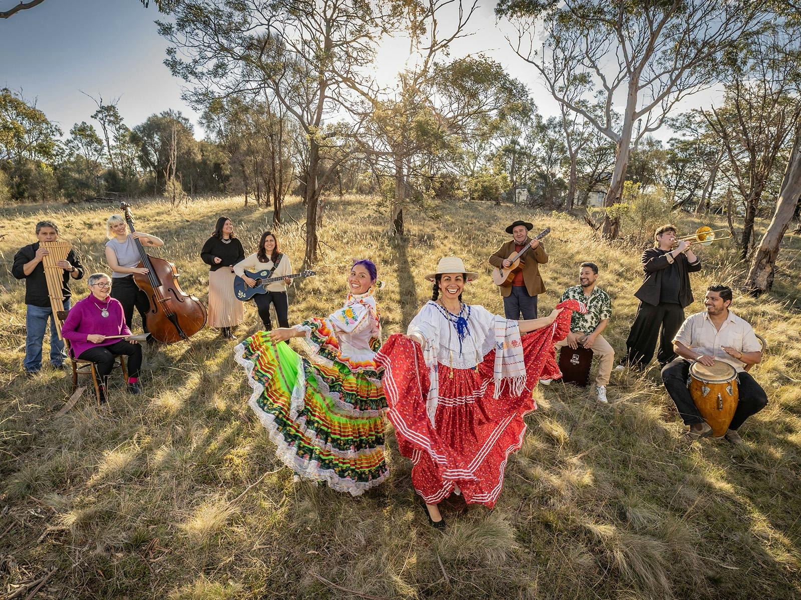 Two smiling women pose outdoors in traditional folkloric dresses, holding out their colorful skirts