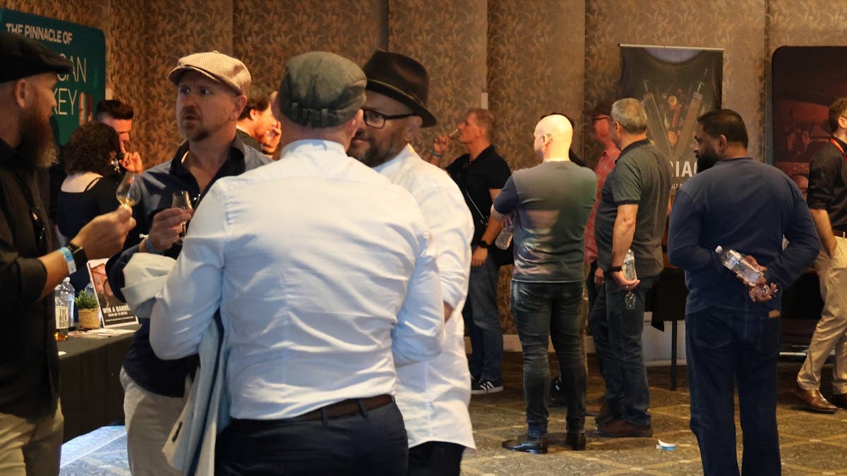 Multiple guests gather in front of stands of whisky brands.