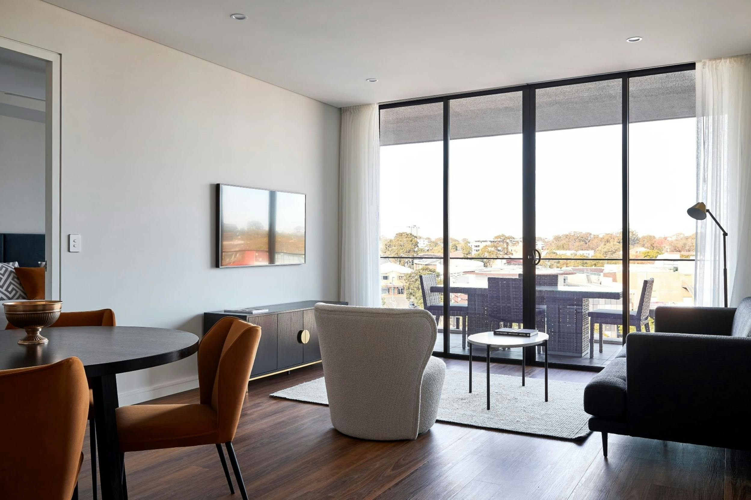 Modern, spacious living and dining room with warm wood floors, a round black dining table and rust-c