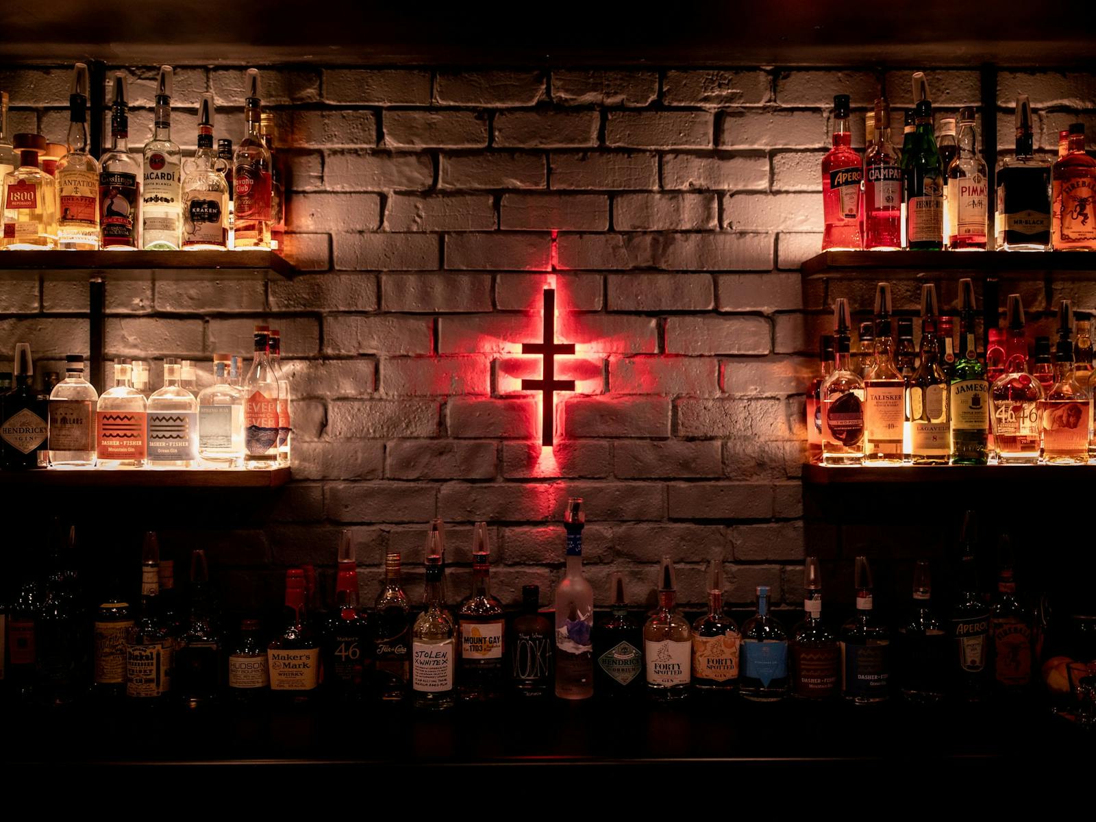 The Altar bar logo glows red on the wall.  Shelves on either side show a variety of alcohol bottles