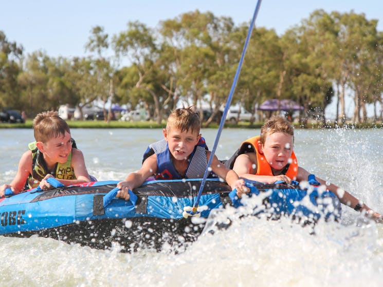 3 young boys riding on a biscuit at speed on Lake Charm