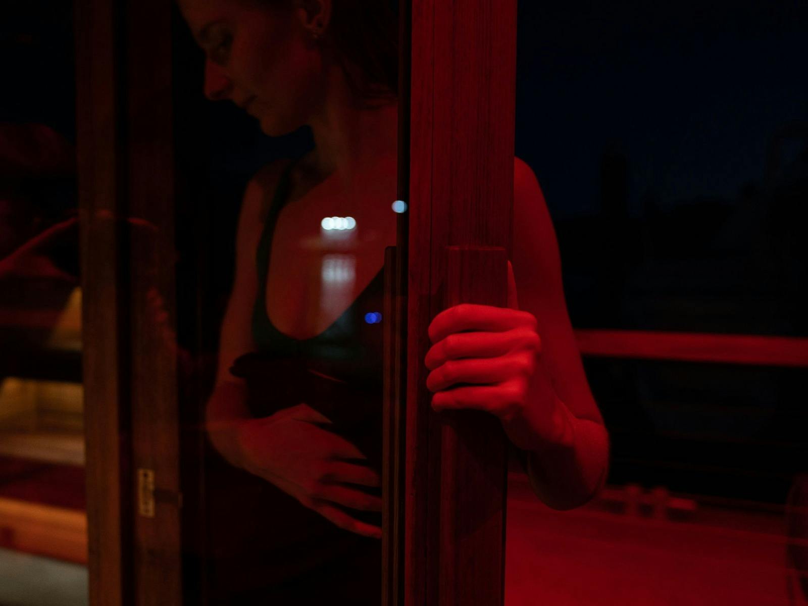 A person opens a wooden door to an atmospheric, red-lit sauna.
