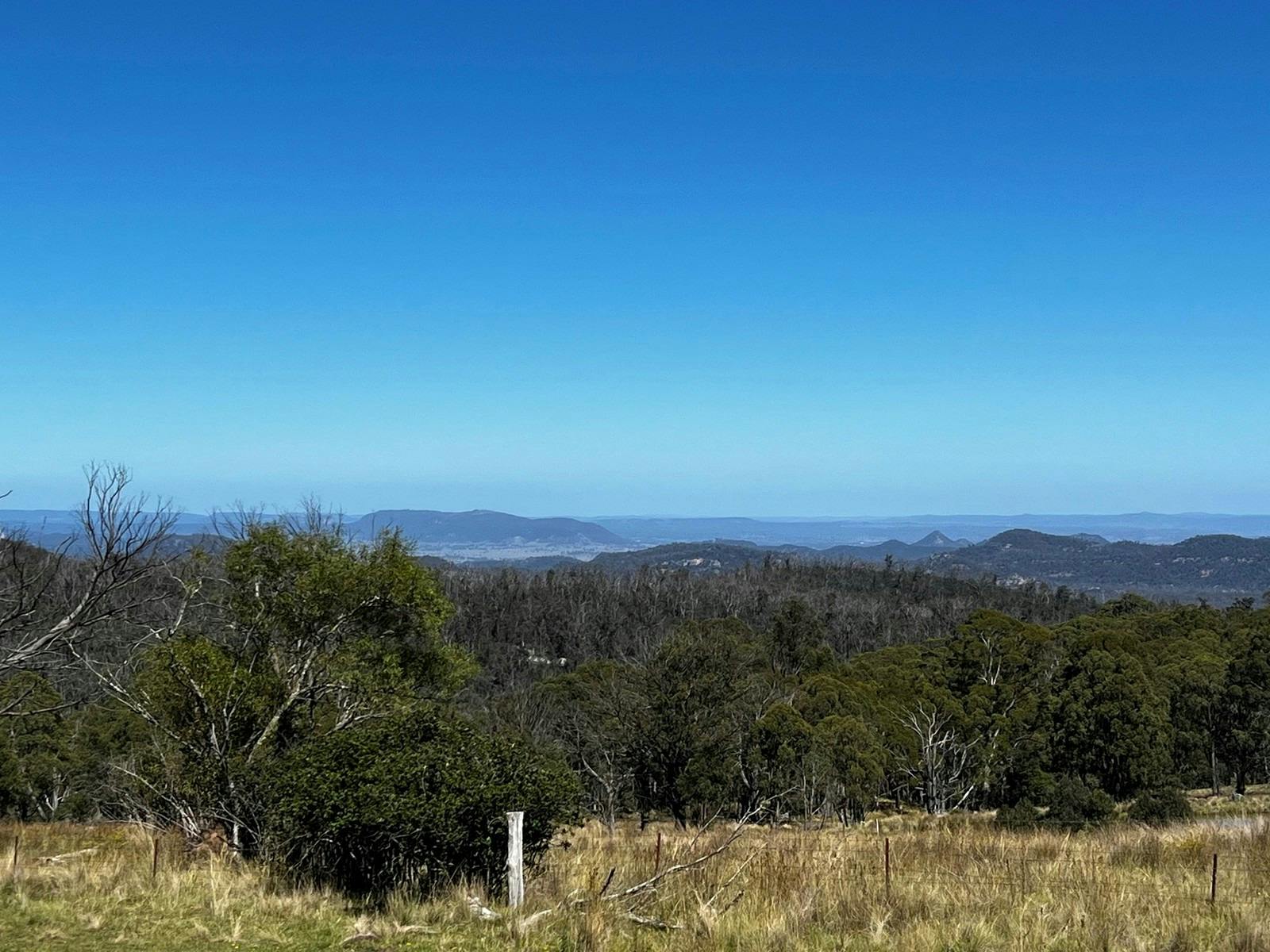 View across bushland, open paddocks and distant mountain ridges under a clear blue sky
