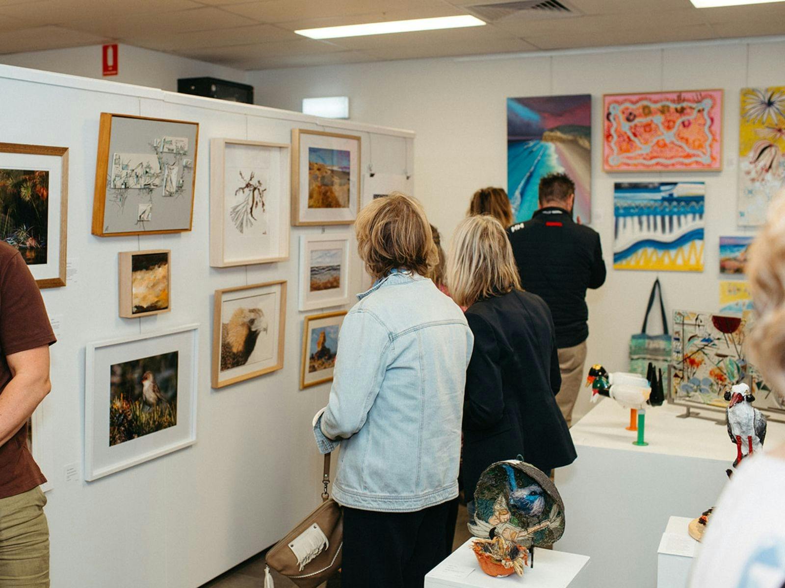 Visitors viewing artworks in a gallery, standing and looking at framed pieces on display walls.