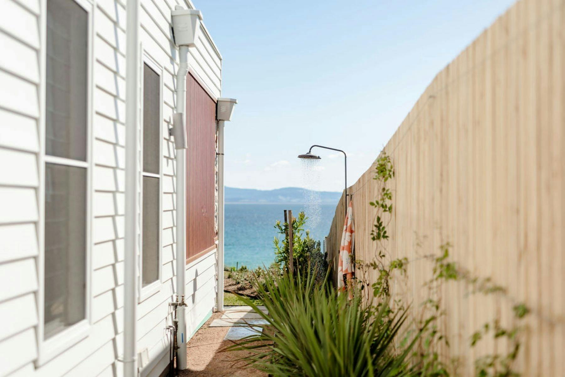 Image of outdoor shower with ocean views in background. Beautiful native plants scattered in image.
