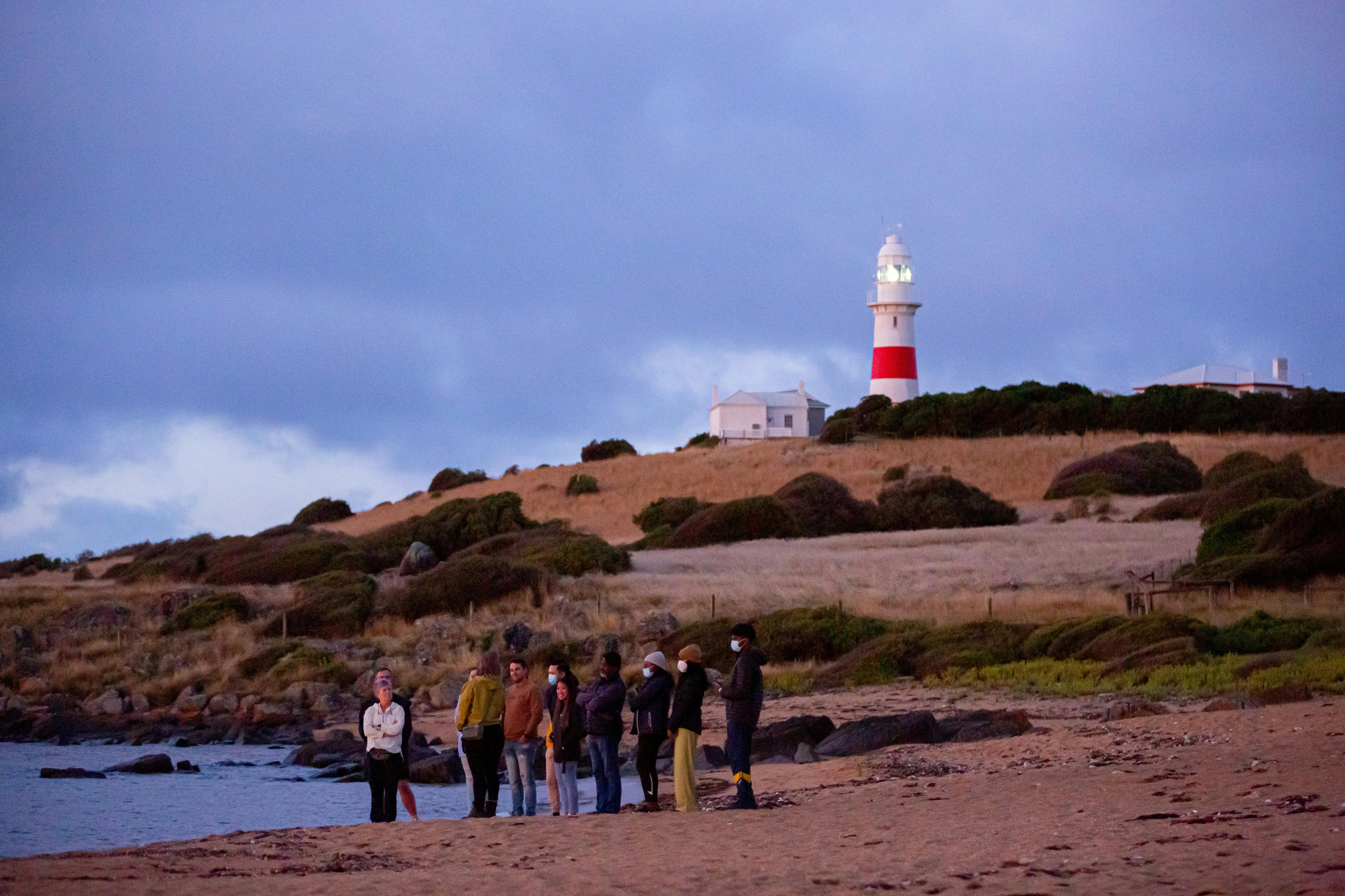 People on a beach early evening with lighthouse in background