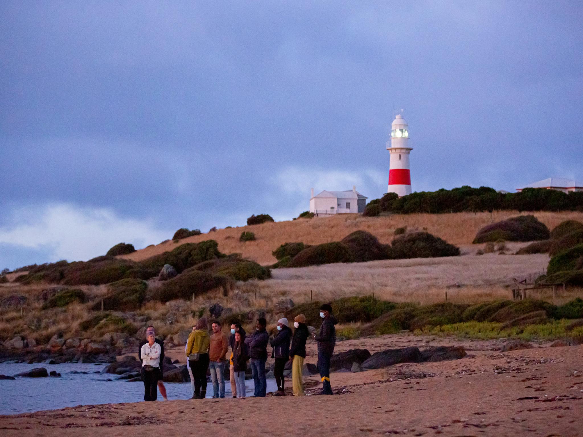 People on a beach early evening with lighthouse in background