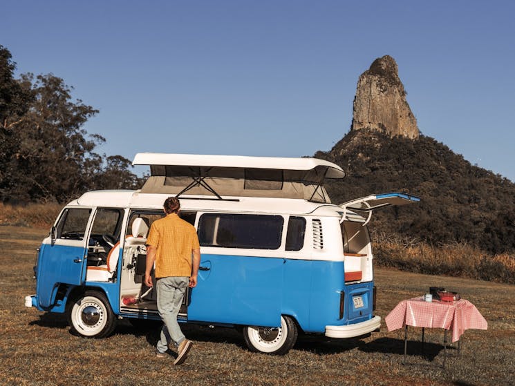 Young camper standing in front of vintage kombi with Glass House Mountains in the background