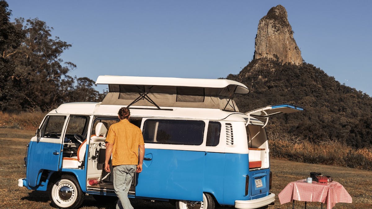 Young camper standing in front of vintage kombi with Glass House Mountains in the background