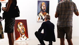 A man is squatting, viewing a portrait leaning on the wall