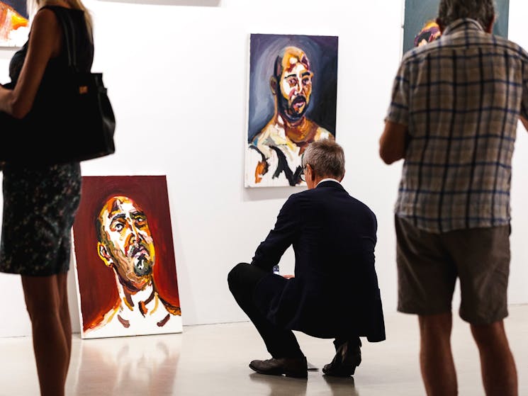 A man is squatting, viewing a portrait leaning on the wall
