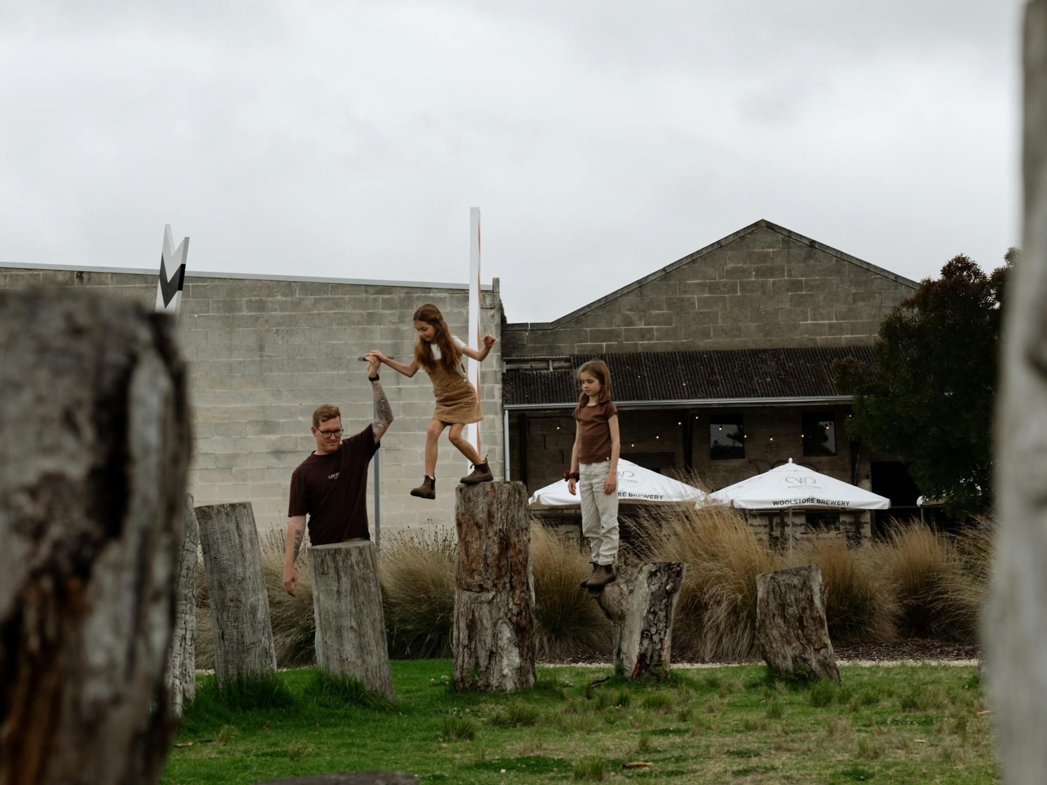 Family playing on posts at reserve with buildings in the background