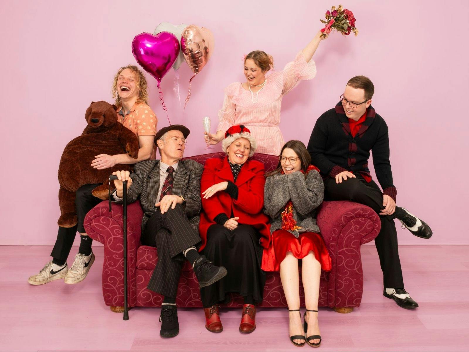 group of 6 people mixed ages sit on a red couch laughing