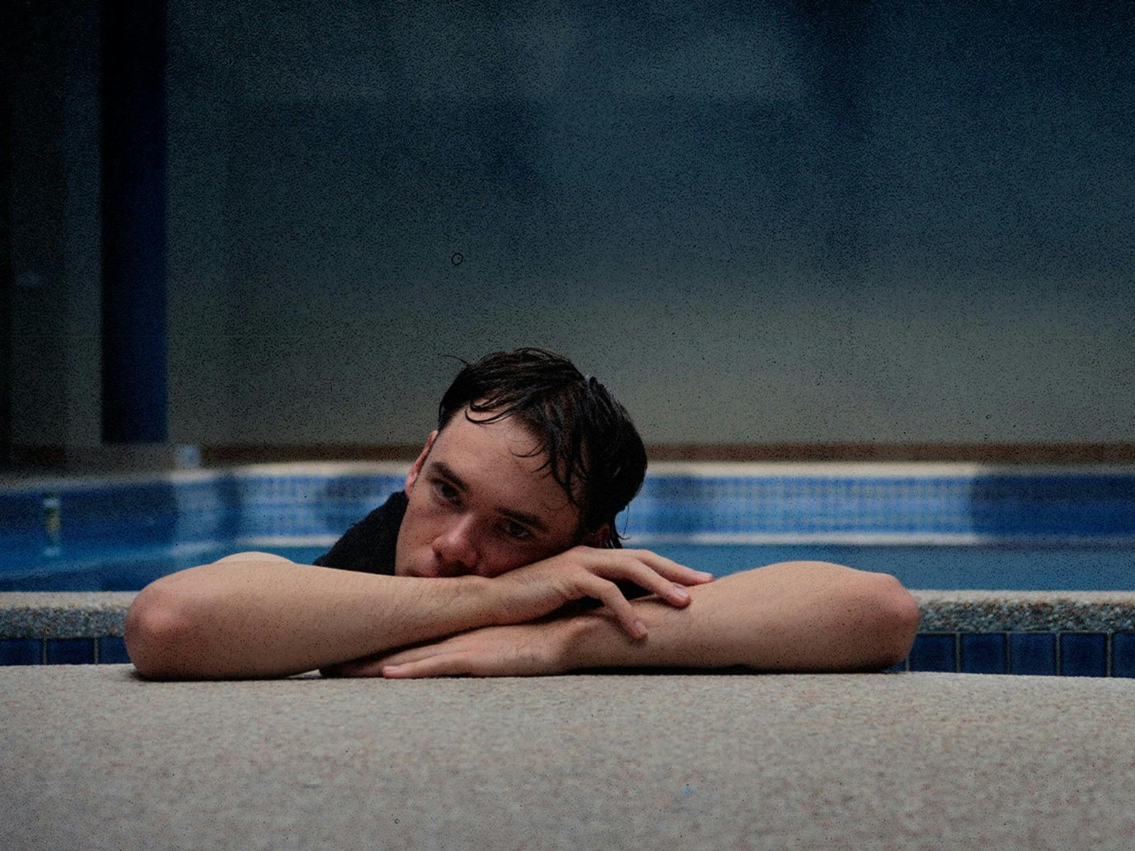 A man sadly lays his head down on his arms. He is leaning on the edge of a pool.