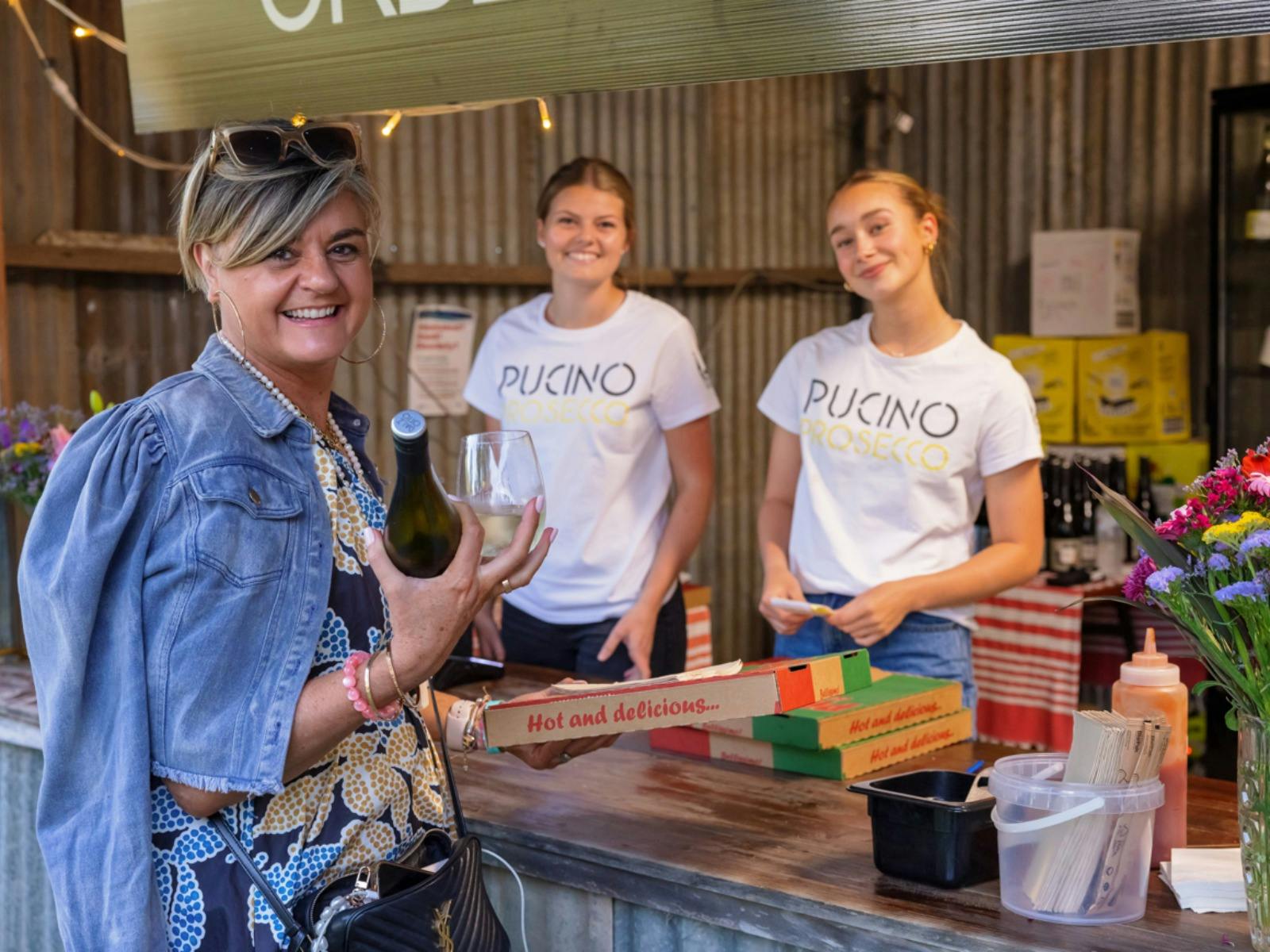Dal Zotto Wines Easter guest standing at Prosecco Bar holding pizza with two smiling bar staff