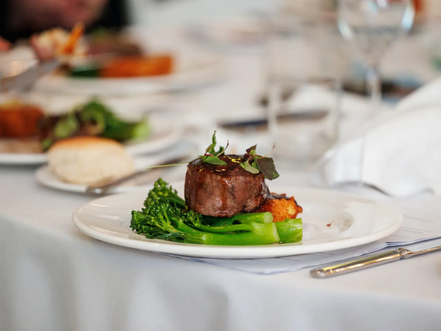 Plated dining meal on a set table. Lamb rump and fresh vegetables.