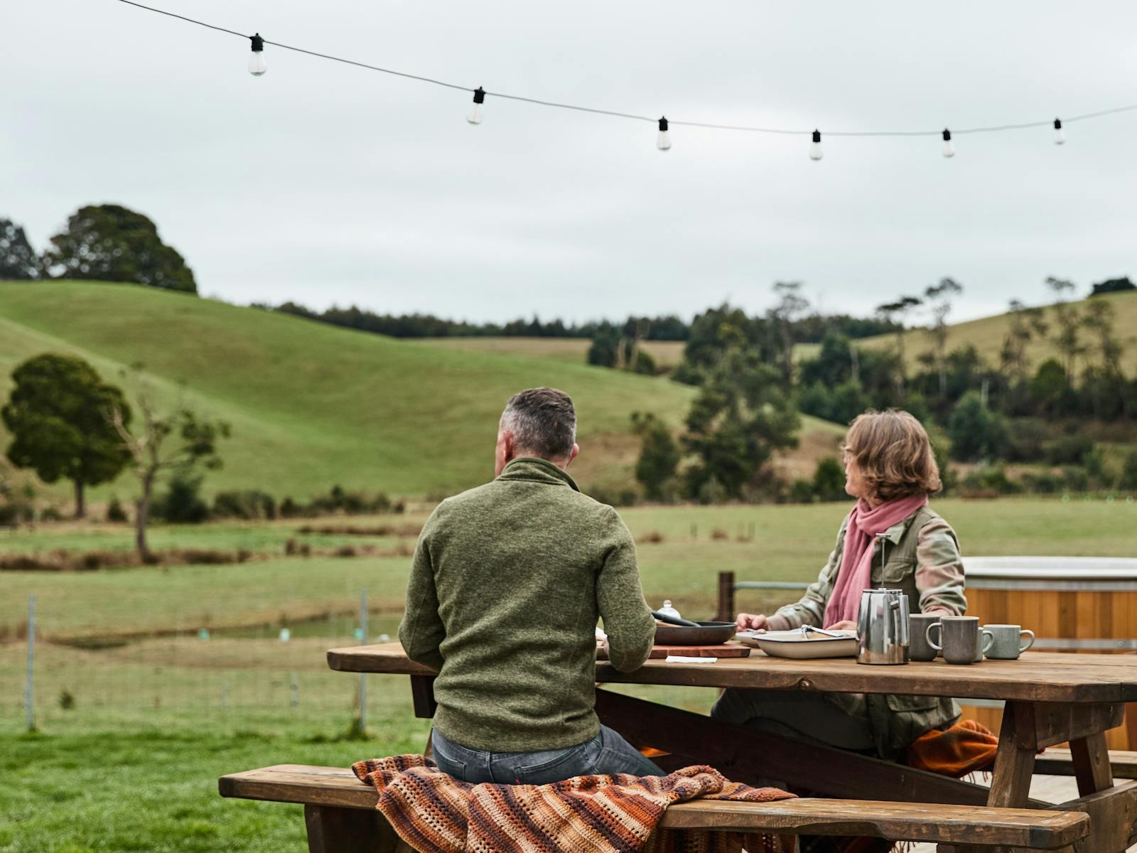 Man and woman sitting at pincic table looking out at paddocks and hills