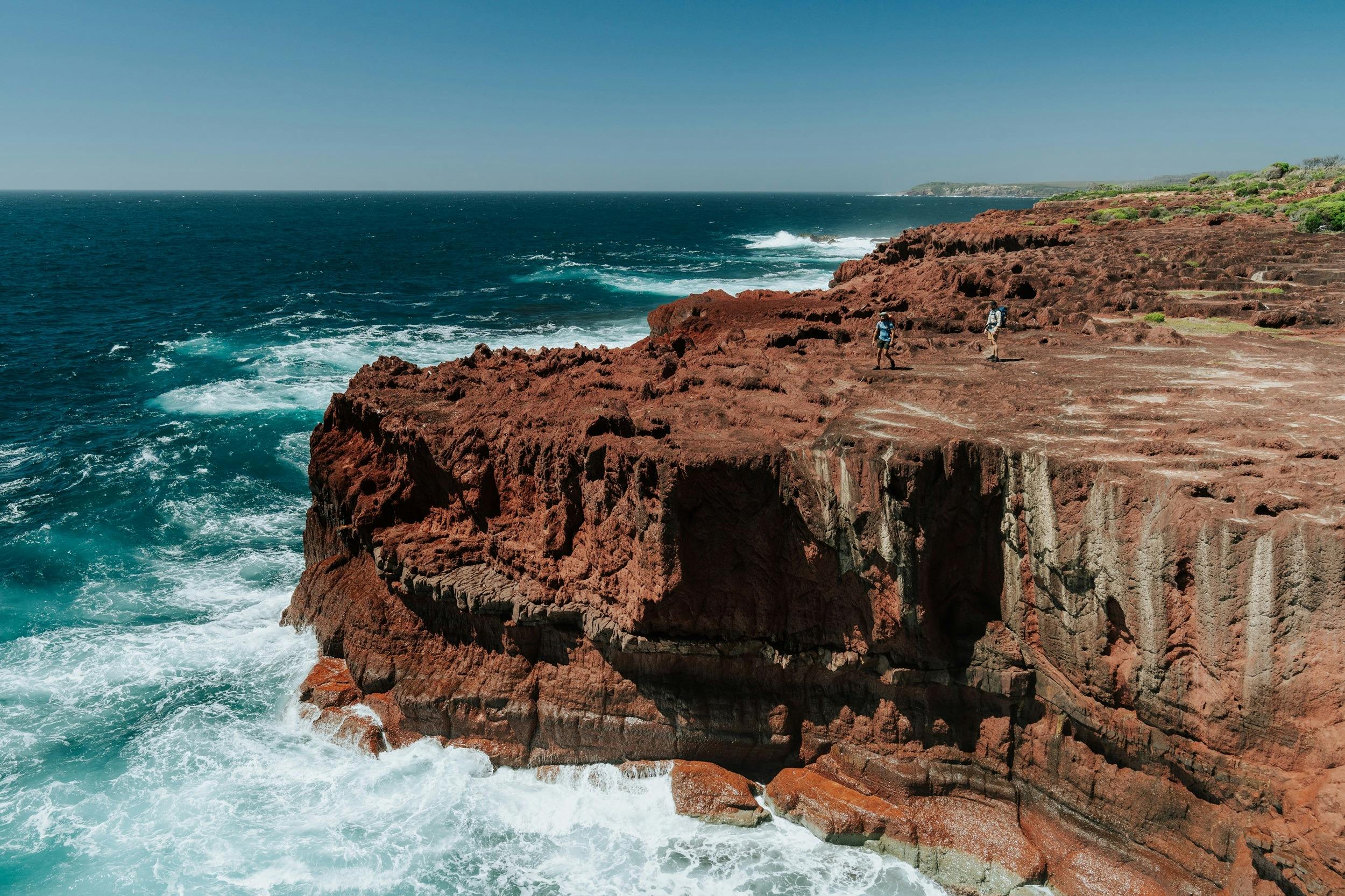 Two walkers on a red rock platform on the Light to Light Walk..