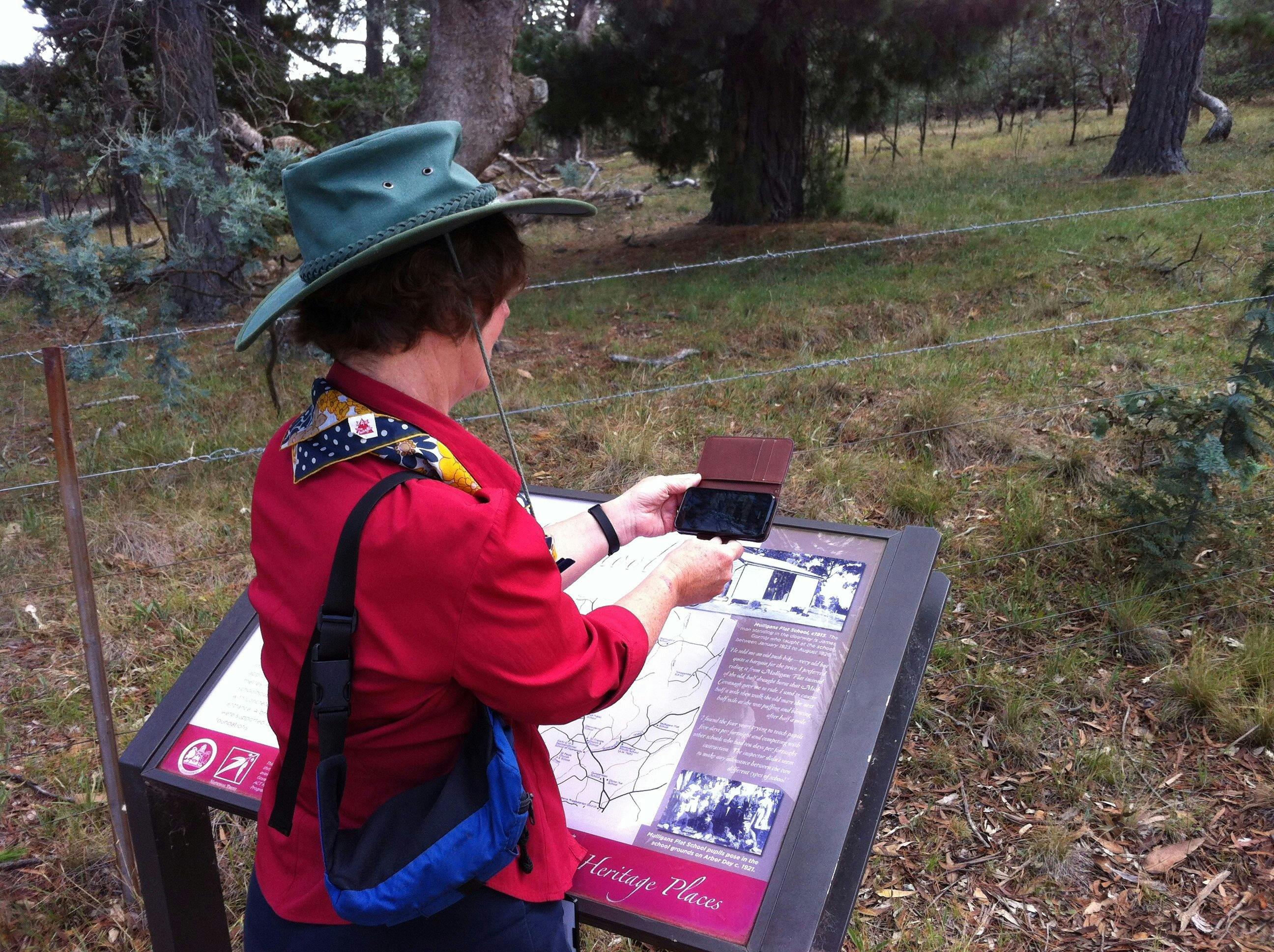 Woman holding smart phone in front of image on sign located in the bush