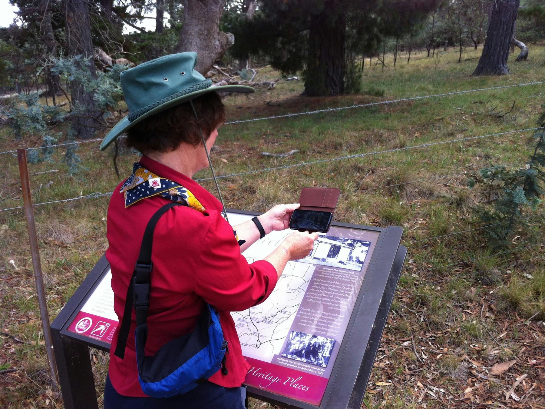 Woman holding smart phone in front of image on sign located in the bush