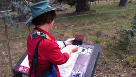 Woman holding smart phone in front of image on sign located in the bush