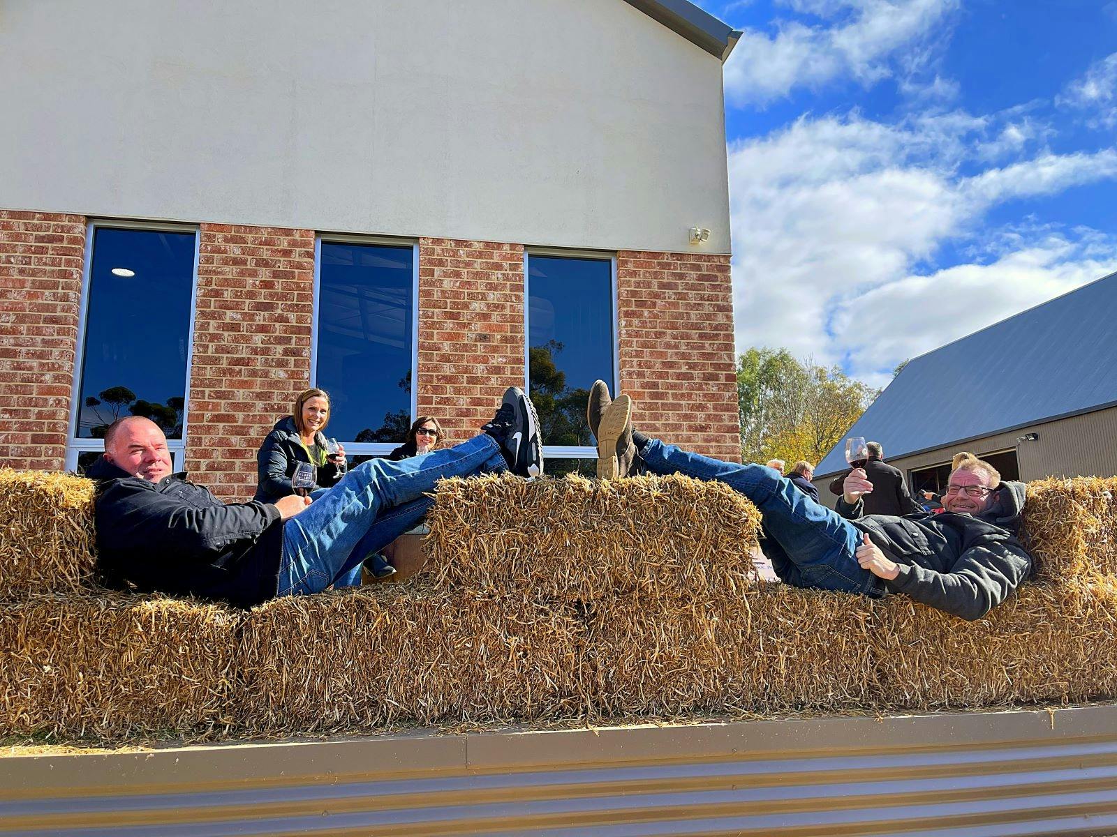men reclining on hay bales in in front of barrel store