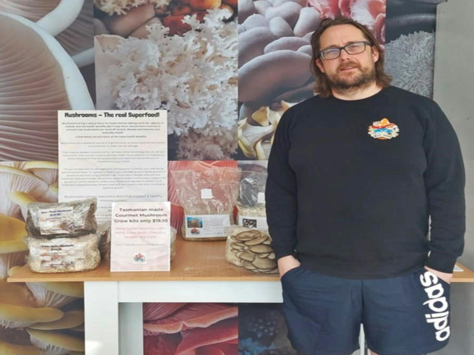 Table with mushroom grow kits with a man in a black jumper standing to the right
