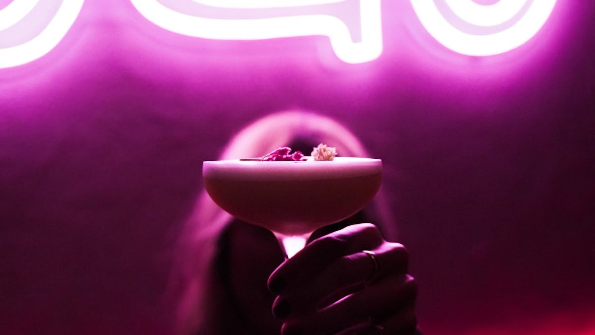 In front of the restaurant sign, a woman holds the signature cocktail.