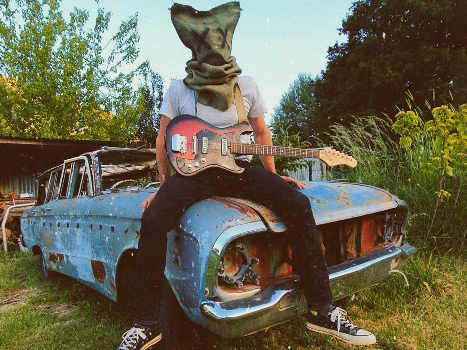 Picture of person sitting on an old car with a bag on their head