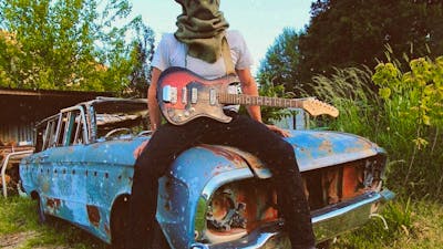 Picture of person sitting on an old car with a bag on their head