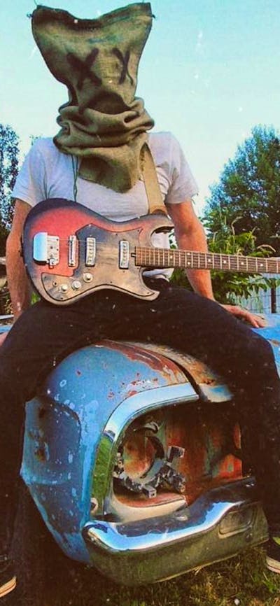Picture of person sitting on an old car with a bag on their head