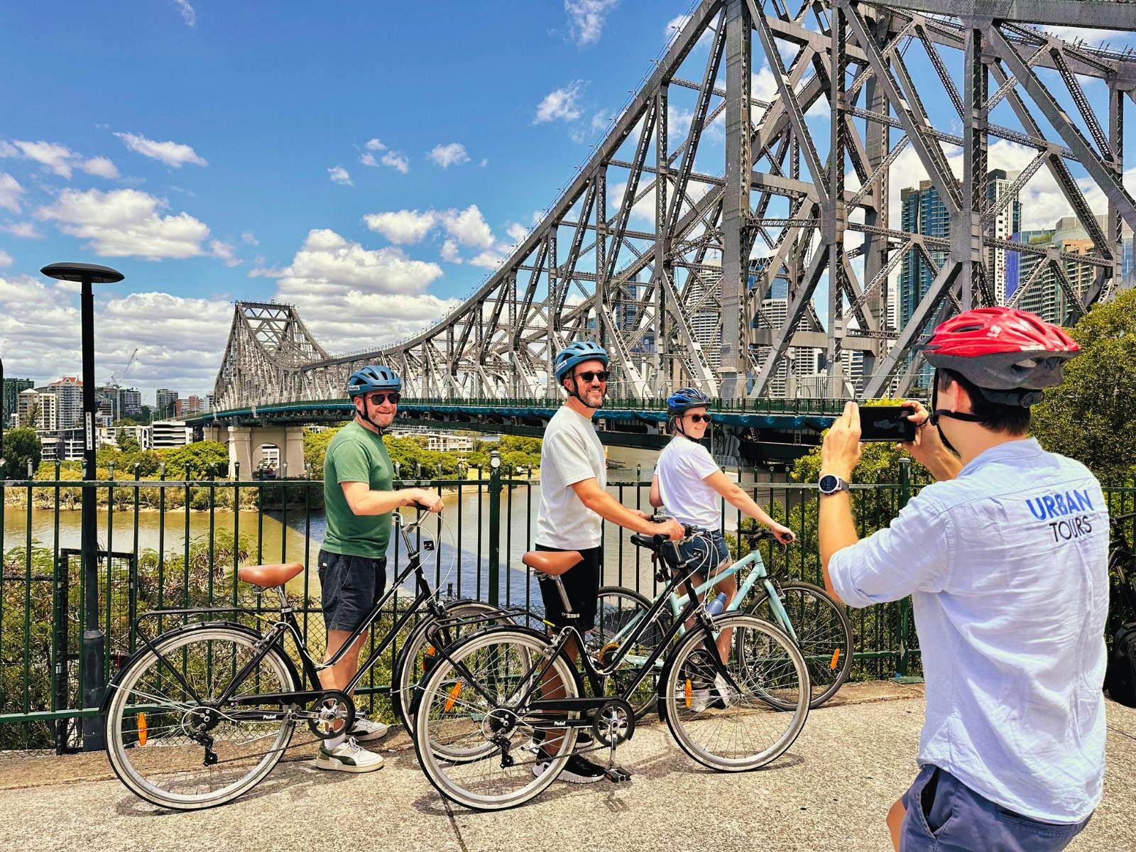 Three people posing for a photograph with a bridge in the back ground, one man taking a photo Three people posing for a photograph with a bridge in the back ground, one man taking a photo