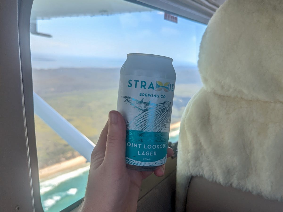 A Straddie Brewing Co Point Lookout Lager beer beside an airplane window