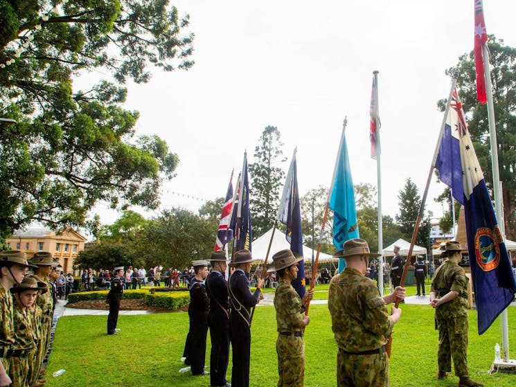 Anzac Day commemoration with flags and community members standing in the background