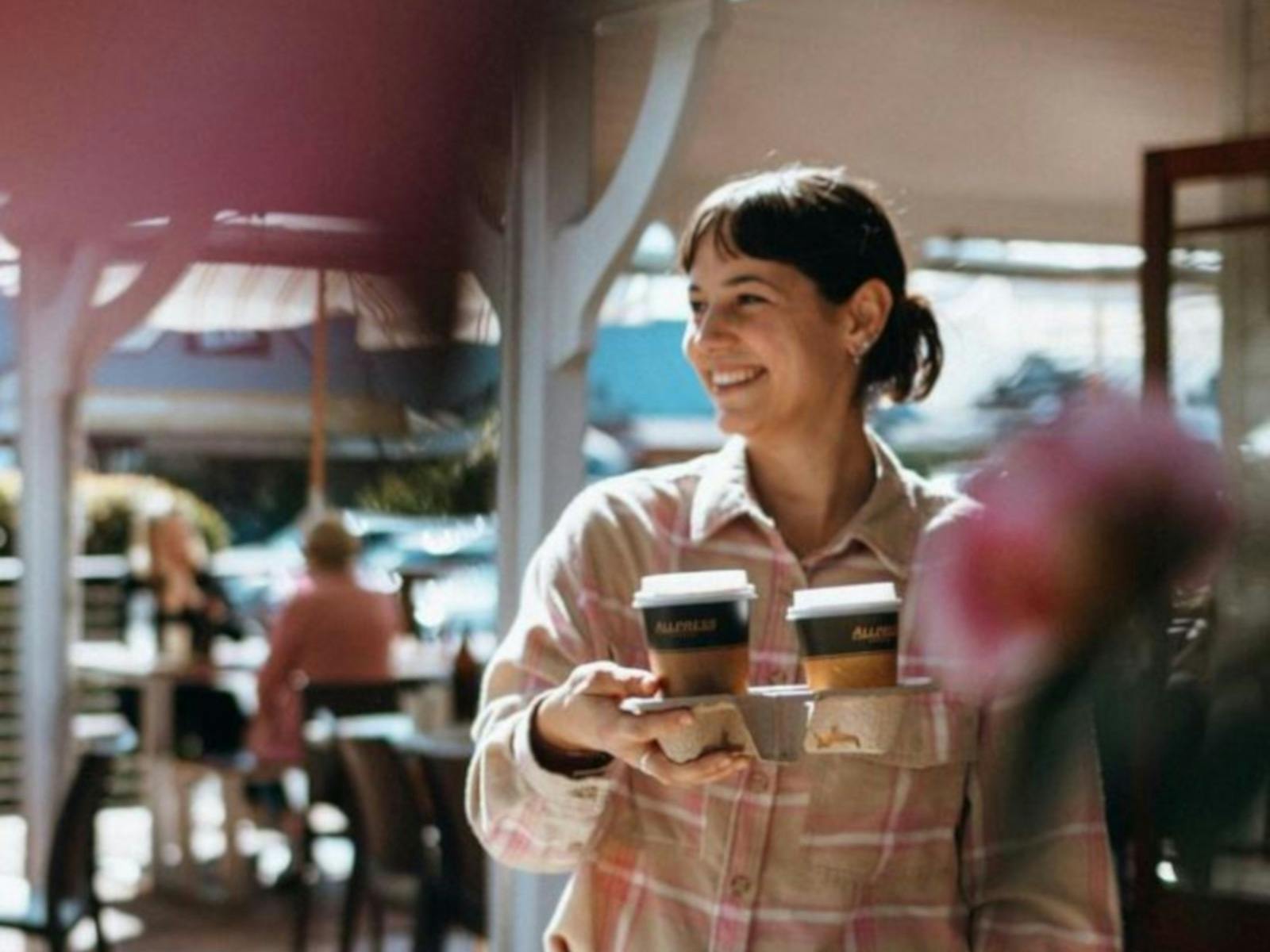 a happy woman carrying takeaway Allpress coffeees