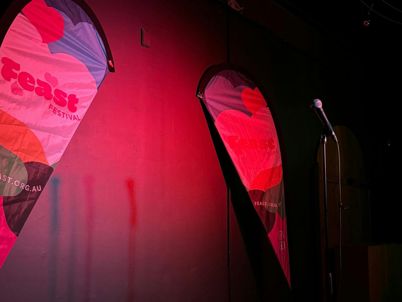 A mic stand on a stage with pink lighting and Feast Festival banners, awaiting a performer.