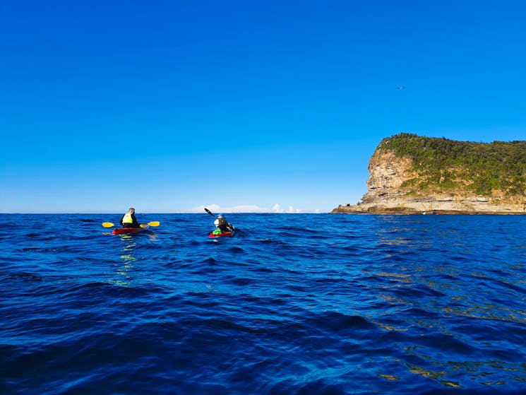 Two kayak paddlers are heading into the open sea with Lion Island in the background.