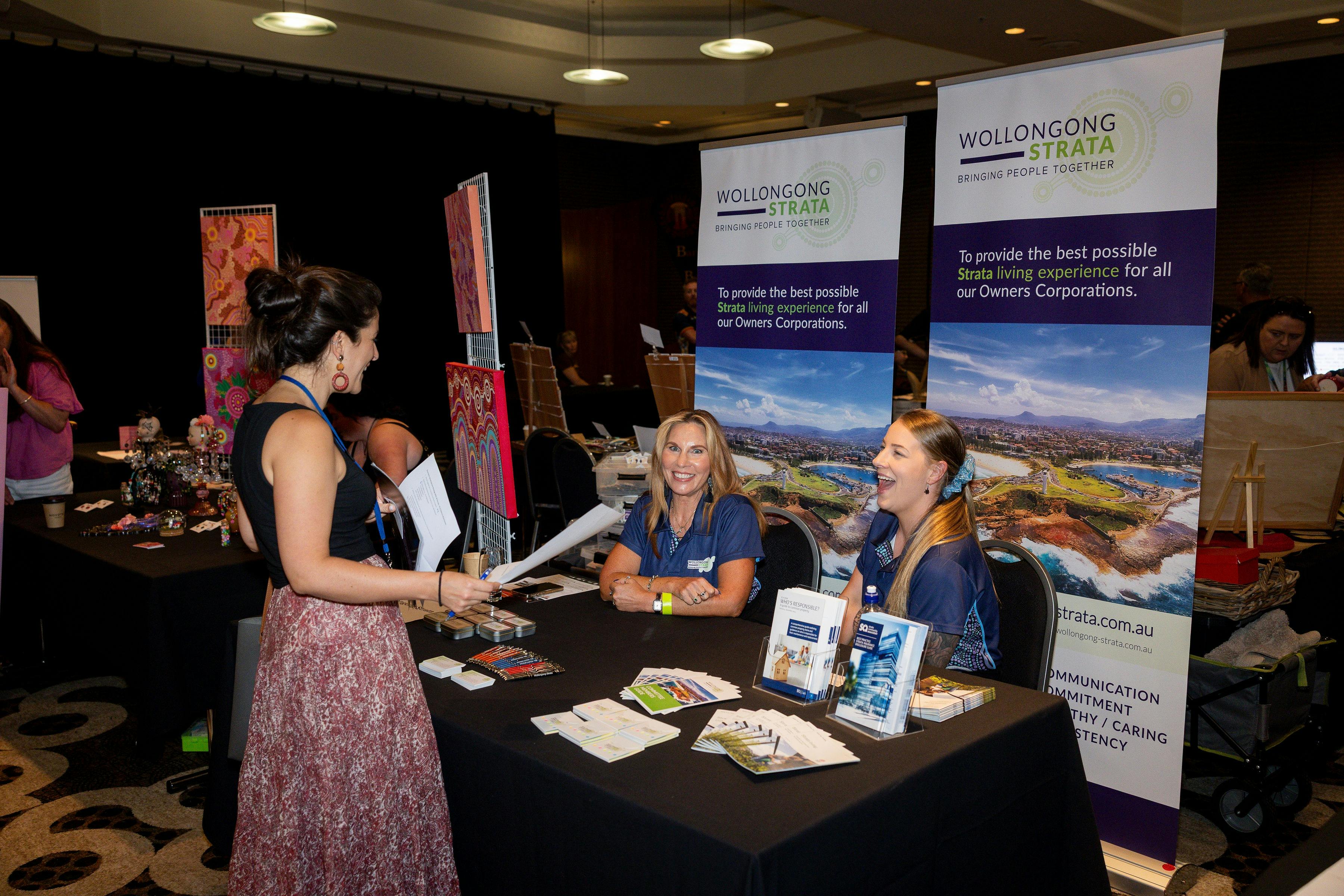 A woman talking to 2 staff members of Wollongong Strata Management at their stall
